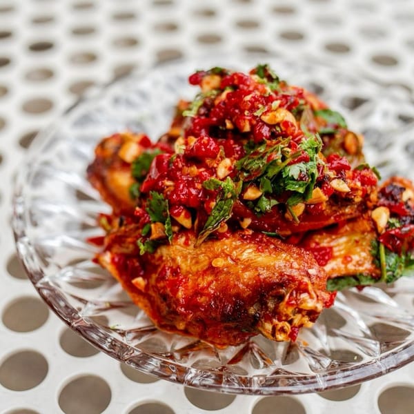 Crispy chicken wings topped with a vibrant red chili and herb relish on a clear glass plate.