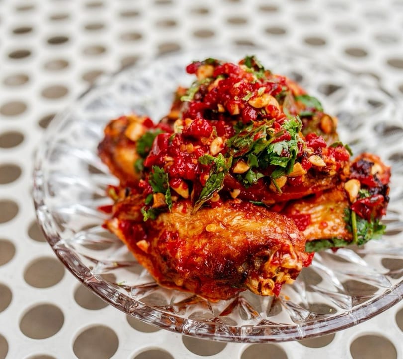 Crispy chicken wings topped with a vibrant red chili and herb relish on a clear glass plate.