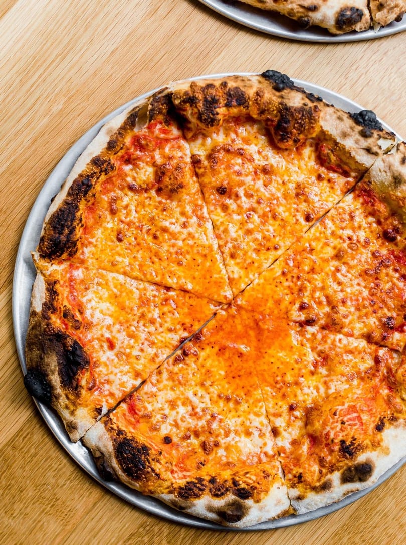A freshly baked, sliced cheese pizza with a bubbly, charred crust on a metal pan.