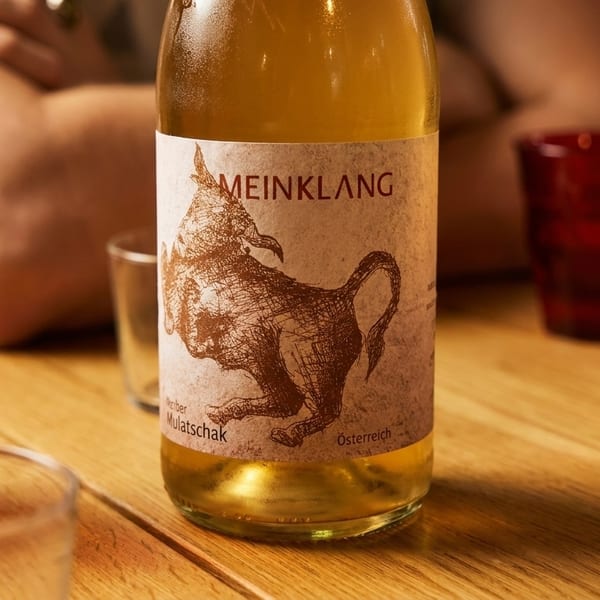 A bottle of Meinklang wine with a bull on the label, surrounded by red glasses on a wooden table.