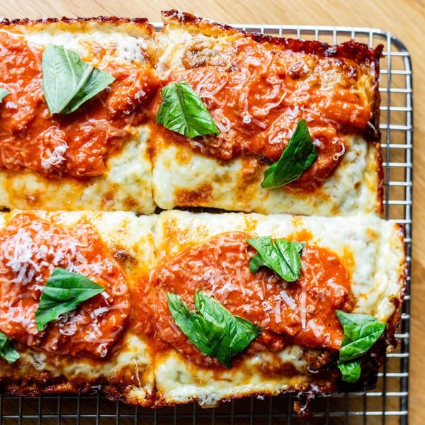Overhead view of four rectangular Detroit-style pizza slices with red sauce, cheese, and basil.