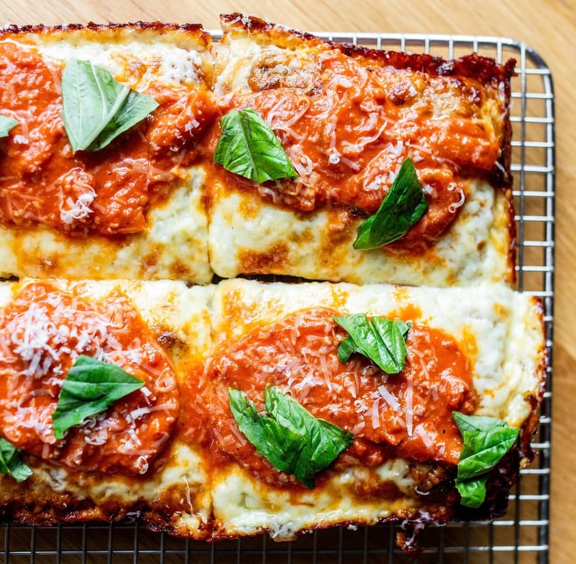 Overhead view of four rectangular Detroit-style pizza slices with red sauce, cheese, and basil.